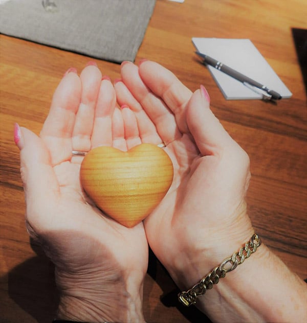 Herz aus Holz wird von zwei Händen gehalten